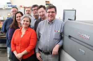 The staff of New Mexico State Printing & Graphic Design Services gathers in front of one of the in-plant&rsquo;s new Ricoh Pro C9210 color printers. From left: Joey Trujillo, Tracey Gallegos, Nina Armijo, Richard Ross, Jose Medina, Don Johnson, and Rob Newlin.